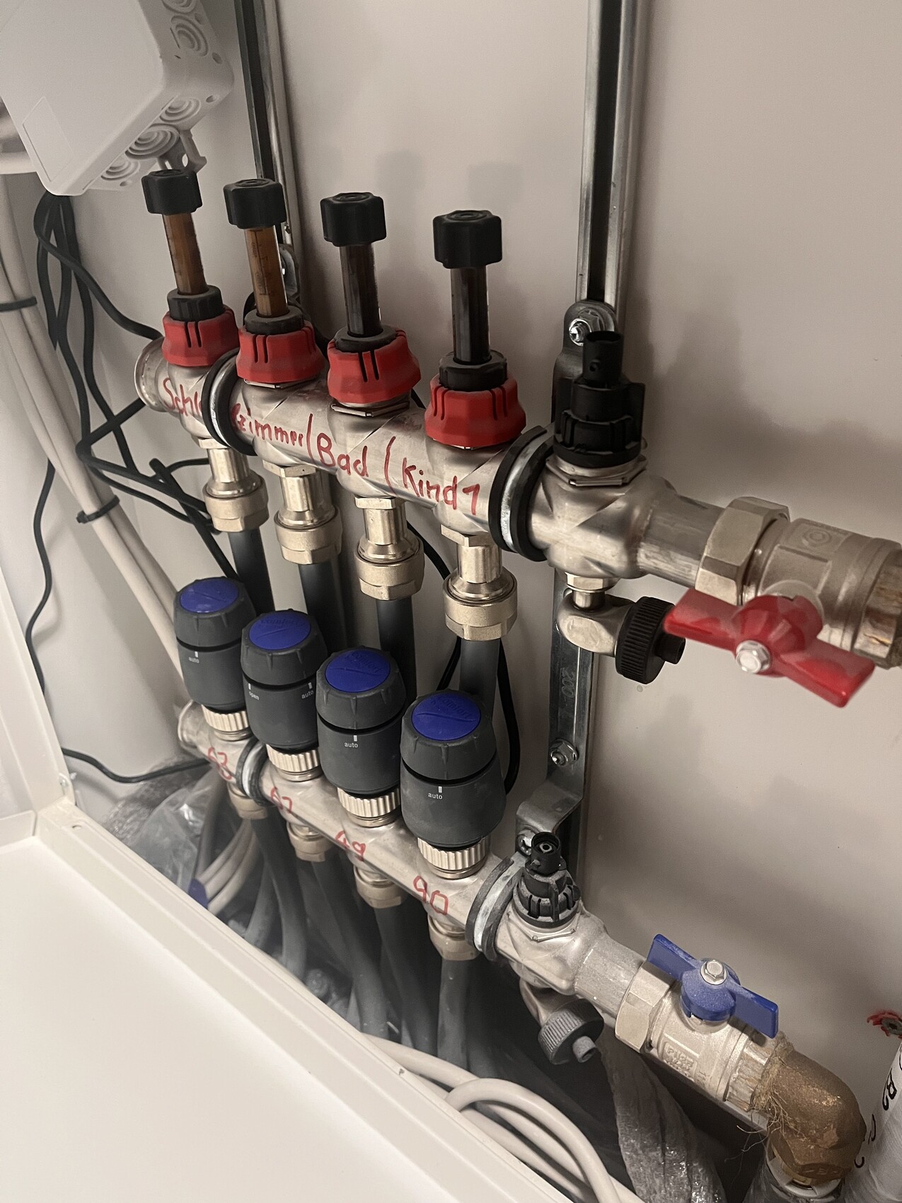Heizungs-Verteiler mit mehreren Zonenventilen, roten Kappen, blauen Drehgriffen und Messleitungen.