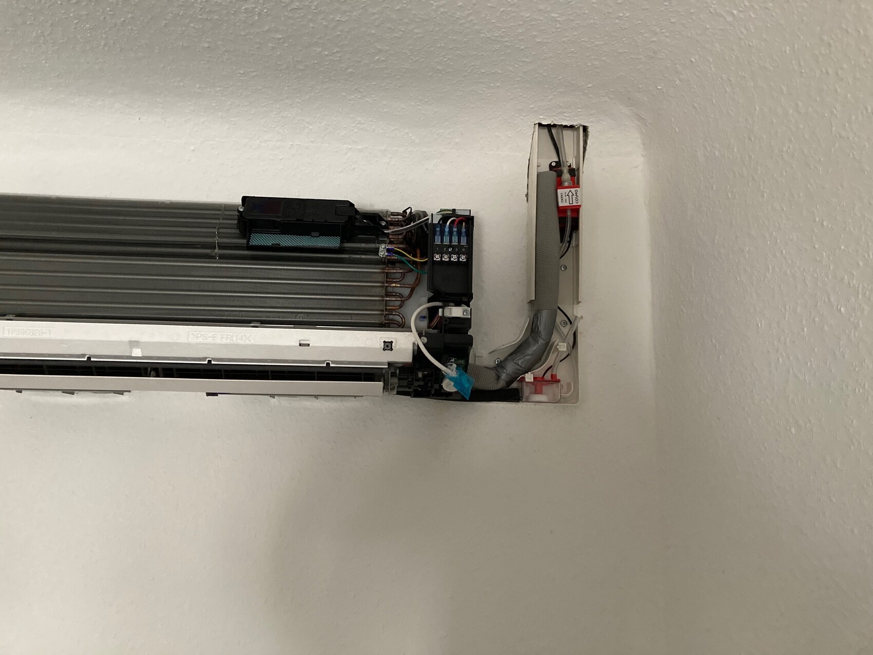 Offene Inneneinheit einer Klimaanlage mit Elektronik, Kupferleitungen und Kabeln an der Wand.