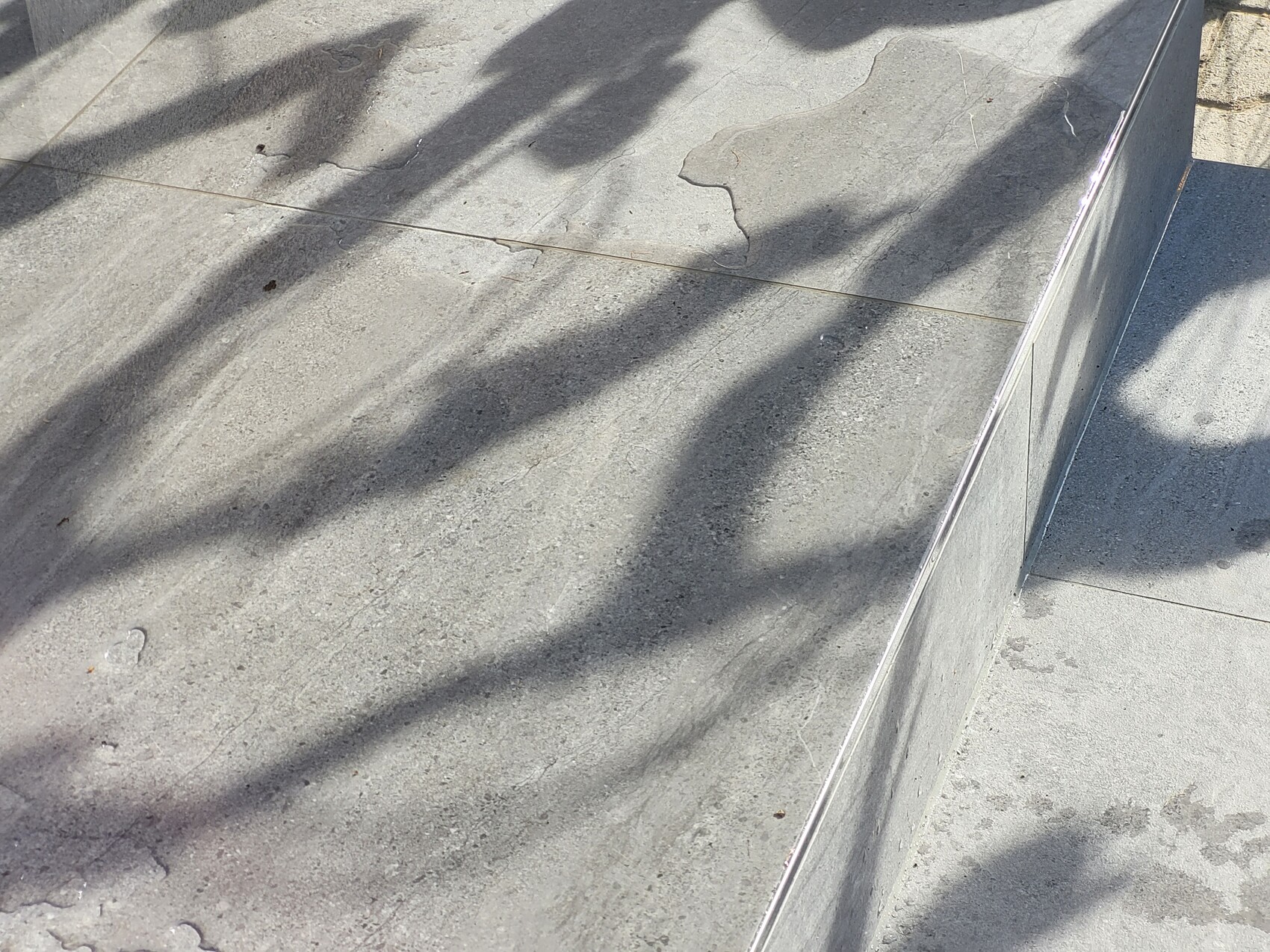 Nahaufnahme einer Betonstufe mit Metallkante, von Schatten überzogen.