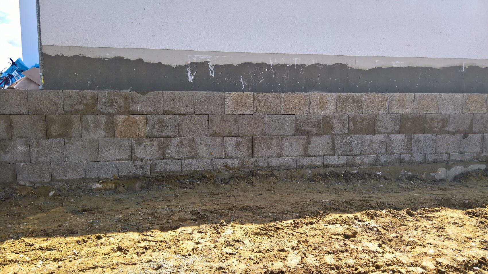 Außenwand aus grauen Betonblöcken über Erdreich; Baustellenboden davor.