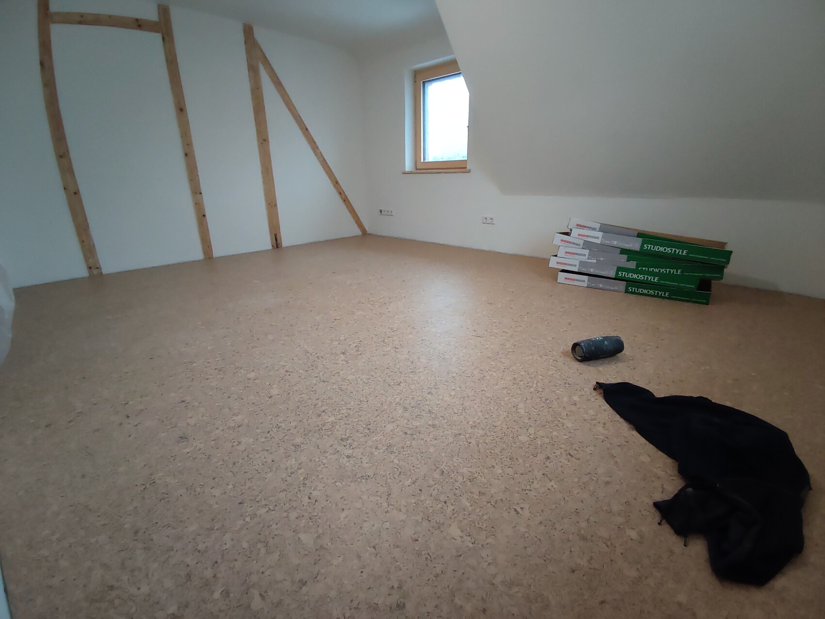 Leerer Dachbodenraum mit Fenstern, Holzbalken, STUDIOSTYLE-Verpackungen und Kleidung auf Boden.