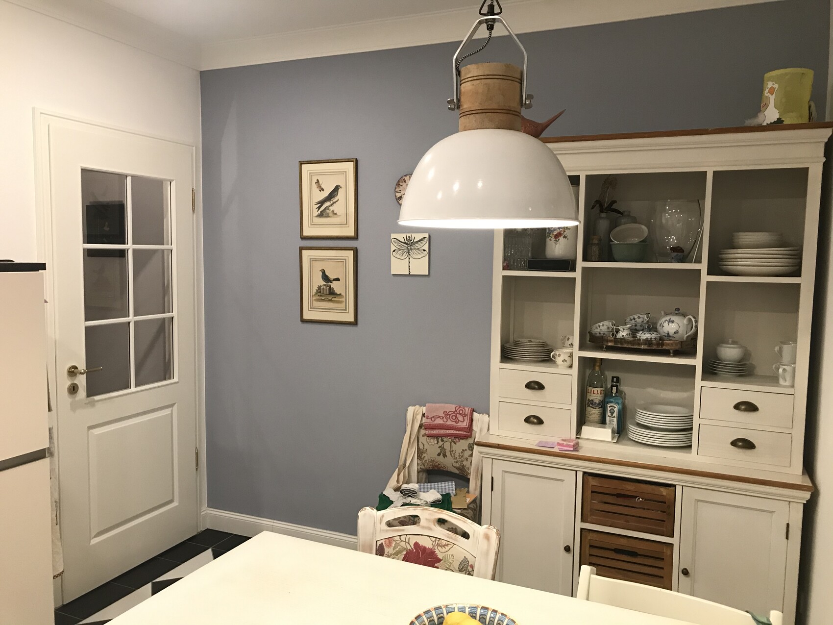 Heller Küchenbereich mit weißem Vitrinenschrank, großer Hängelampe und blauer Wand.
