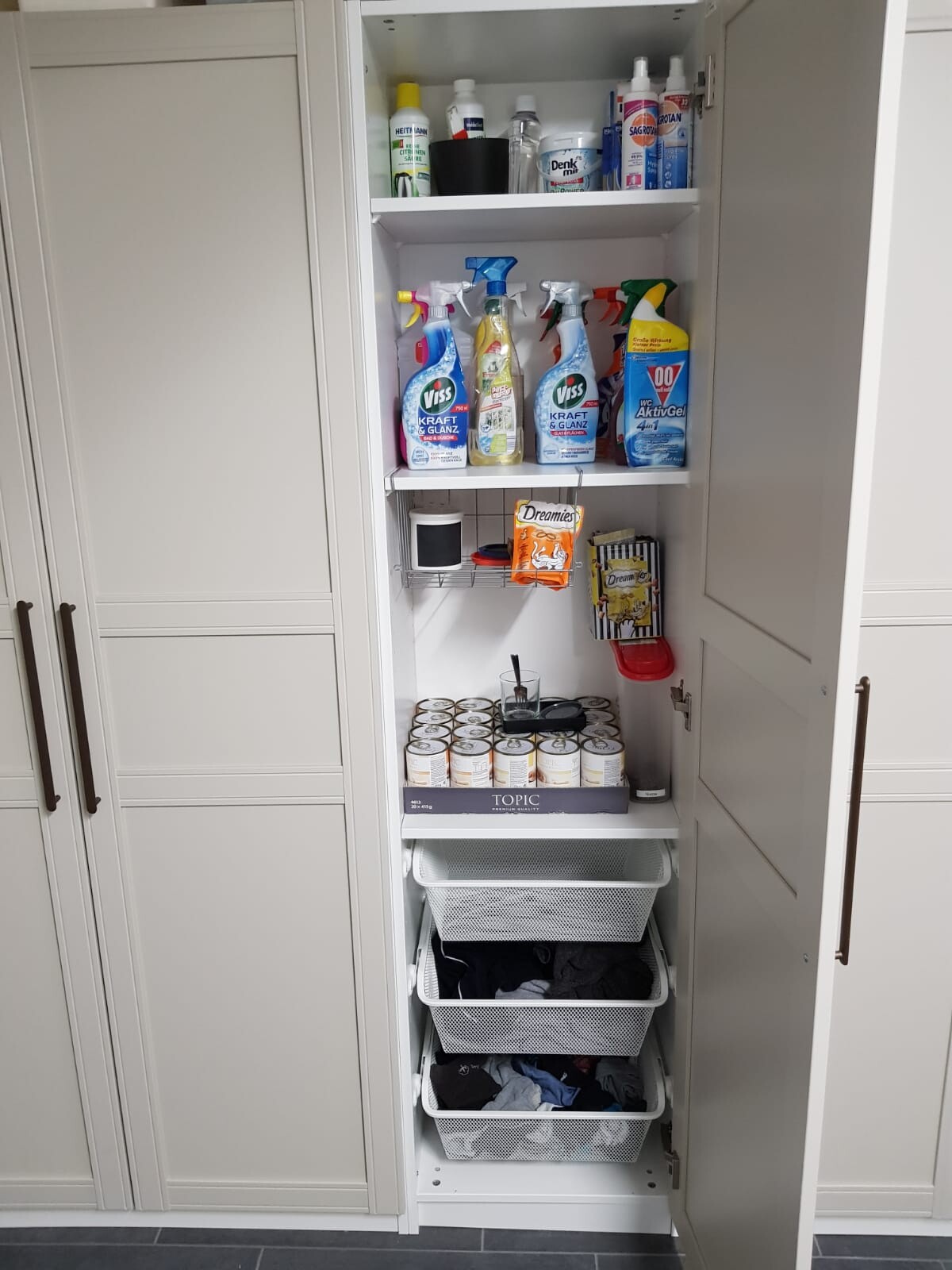 Offener Küchenschrank mit Reinigungsmitteln, Katzenfutter, Dosen und Wäschekörben.