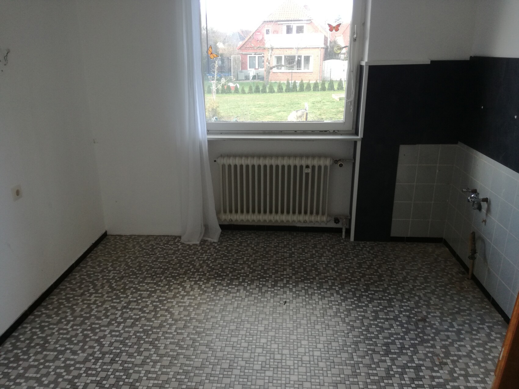 Leeres Zimmer mit Mosaikboden, Heizkörper unter Fenster, Blick auf Garten.