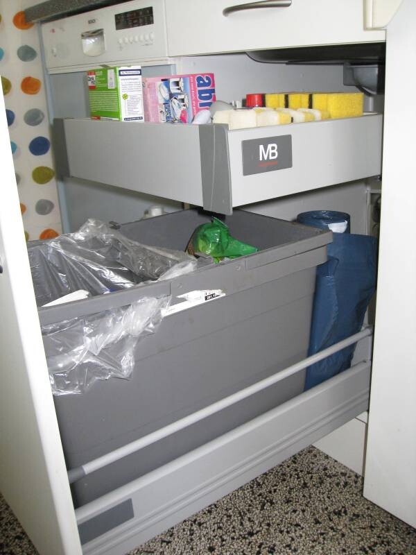Offene Küchenschublade mit Abfallbehältern, Müllsäcken und Reinigungsmitteln.