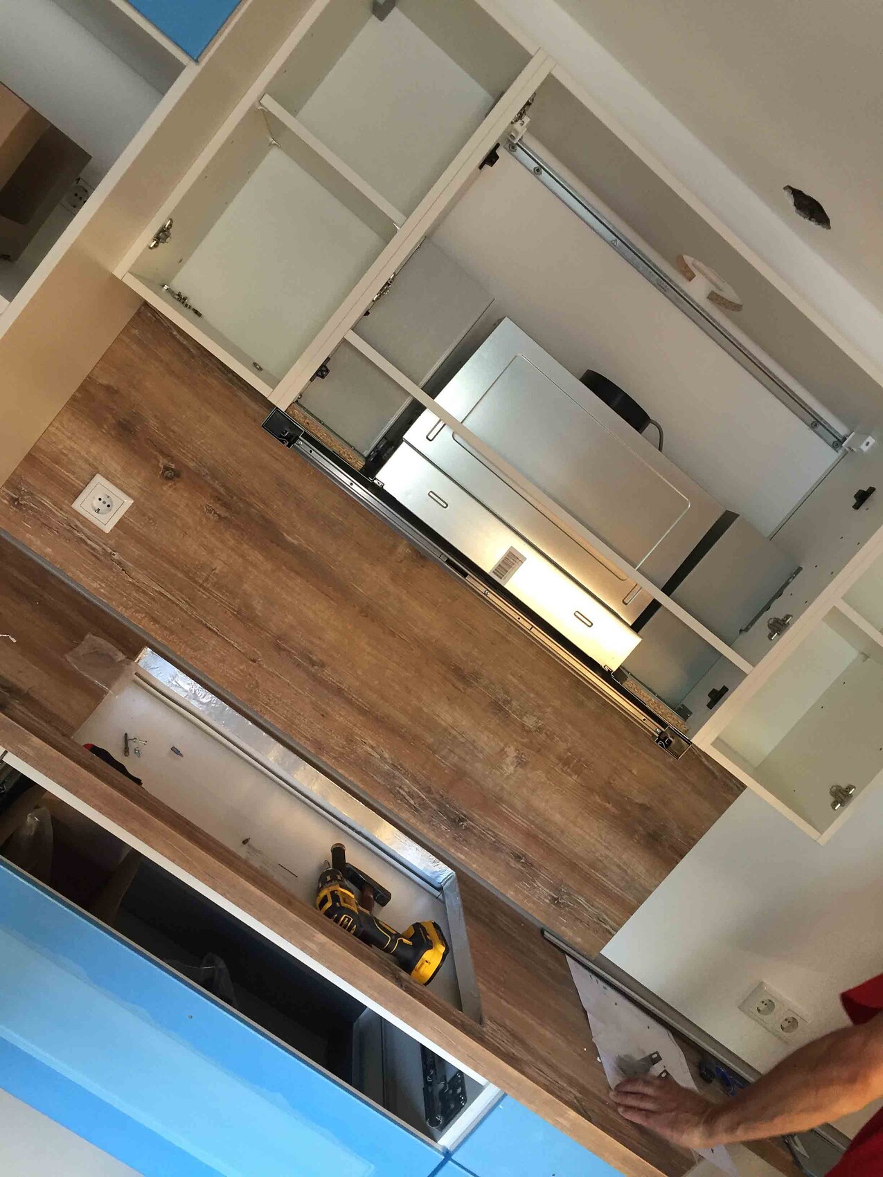 Küche im Bau mit weißen Schränken, Holzfußboden und Bohrmaschine