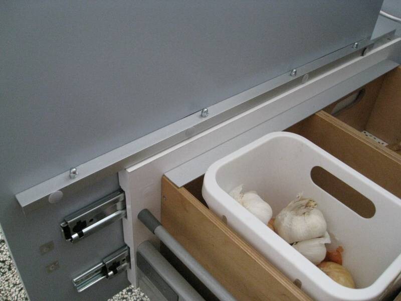 Offenes Metallfach in einer Holzschublade mit weißem Kunststoffkorb voller Knoblauch.
