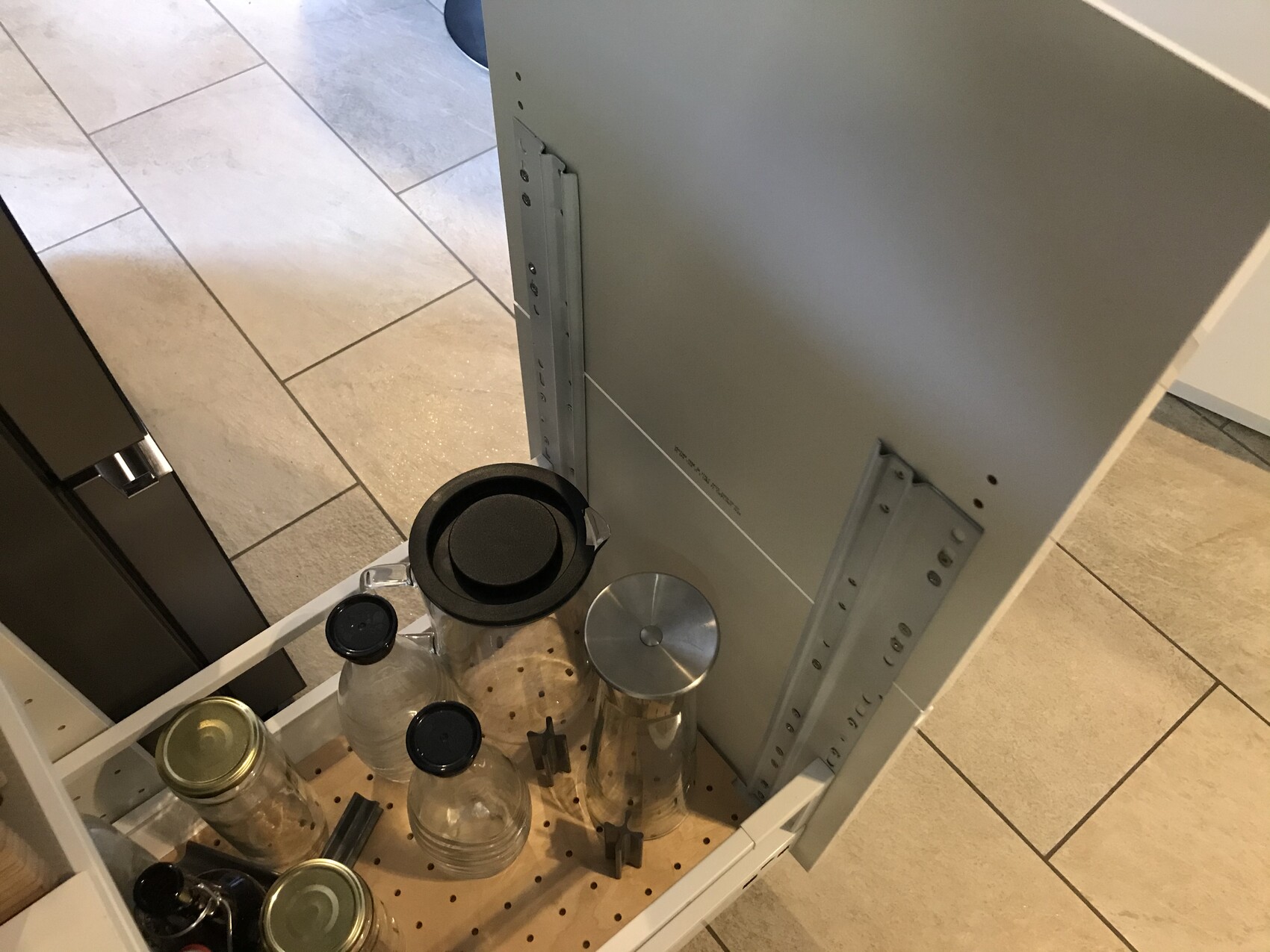 Ausziehbarer Küchenschrank mit Glasbehältern und Deckeln auf Lochboden.