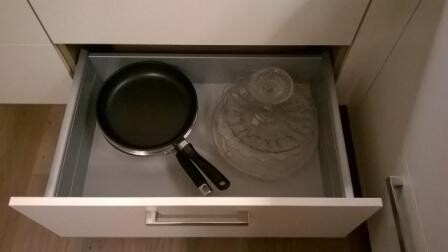 Offene Küchenschublade mit Pfanne und Glasdeckel.