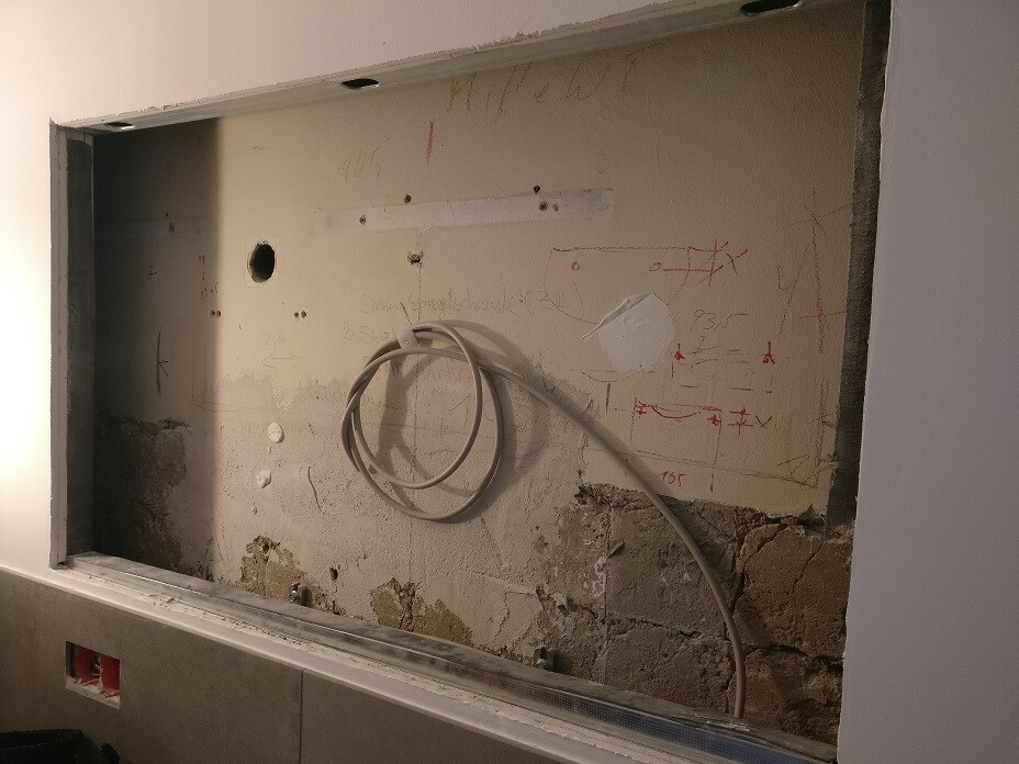 Aufgeschnittene Küchenwand mit freiliegendem Putz, Kabelschlaufe und Wandskizzen.