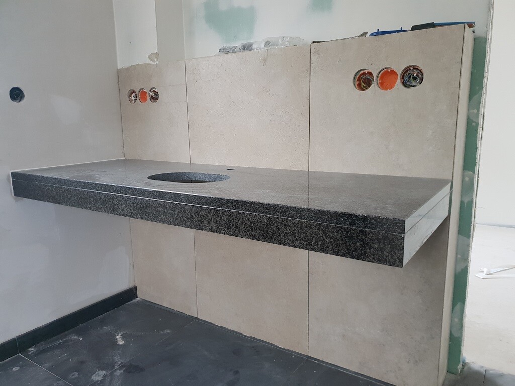 Küchenarbeitsplatte aus schwarzem Granit mit Spülenausschnitt; beige Fliesenwand dahinter.