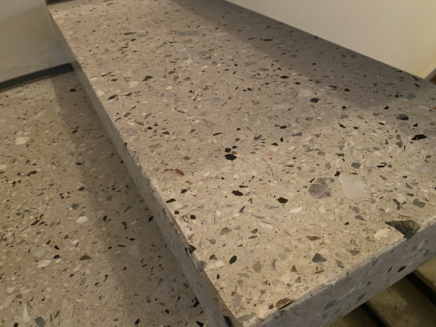 Terrazzo-Arbeitsplatte mit bunten Chips, hellem Grundton, Eckkante sichtbar.