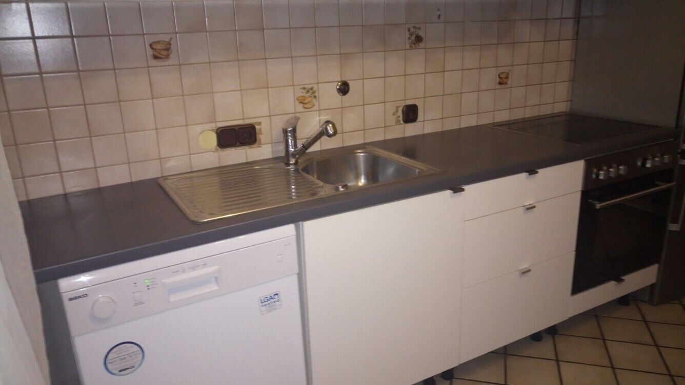 Küche mit Spüle, Geschirrspüler, Herd und weißen Unterschränken vor Fliesenrückwand