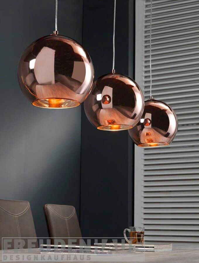 Drei kupferne Pendelleuchten hängen über einem Esstisch; Stühle daneben, Glas auf dem Tisch.