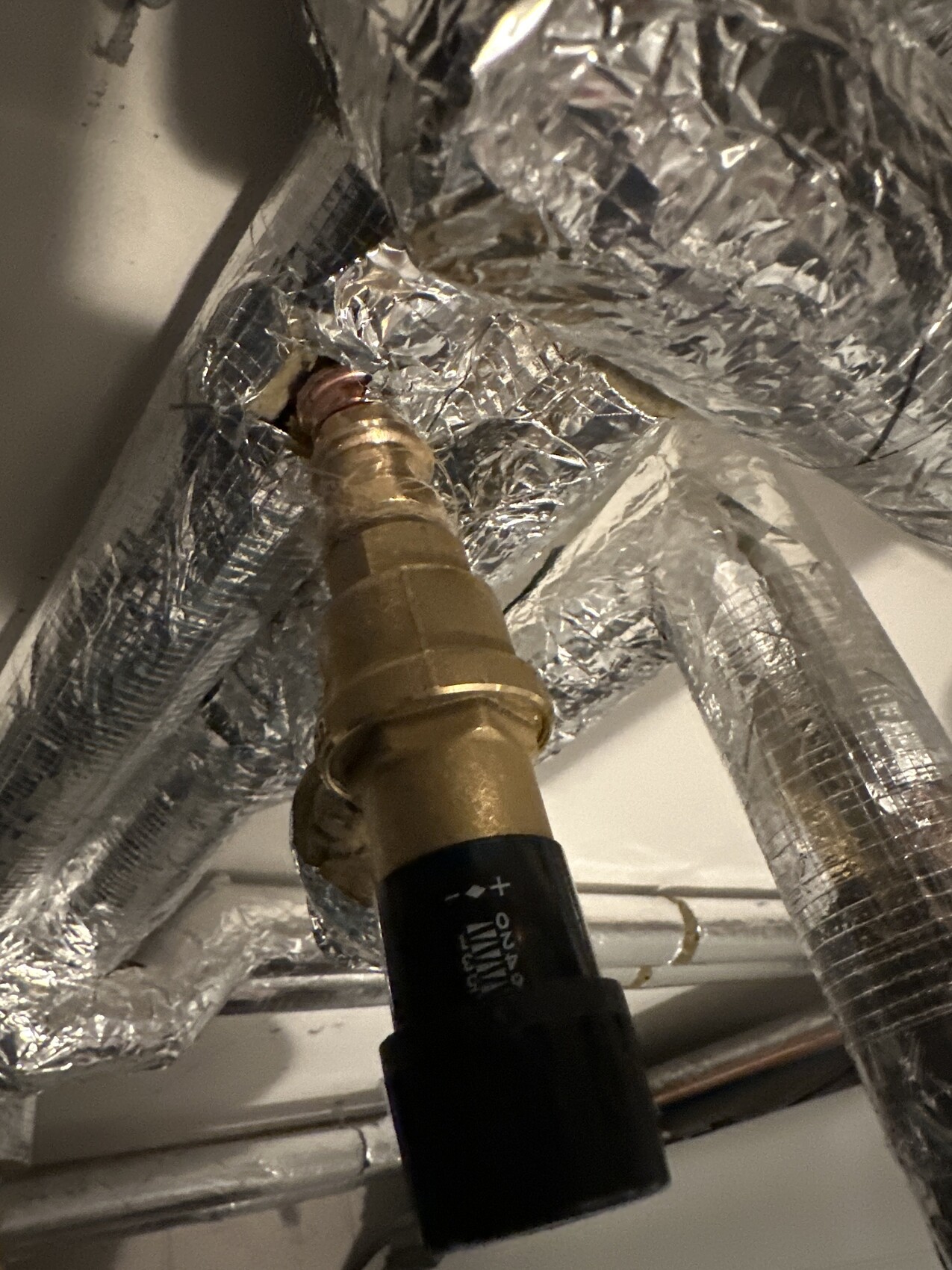 Messing-Absperrventil an einer Rohrleitung, umgeben von Aluminium-Dämmfolie im Installationsbereich.