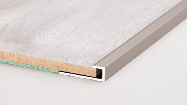 Querschnitt einer Laminat-/Holzplatte mit Metallkante und darunter Kork- und Schaumstoff-Isolierung.