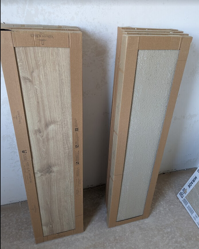 Zwei Verpackungen für Bodenbeläge stehen nebeneinander; links Holzoptik, rechts Grau-Panel.