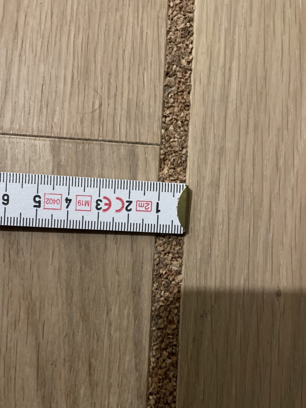 Maßband liegt quer über zwei Holzdielen; sichtbare Fuge zwischen den Dielen, Abstand ca. 2 cm.
