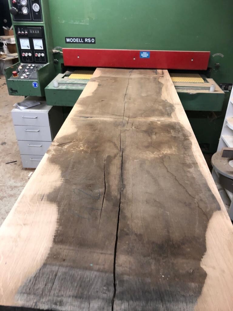 Langes Holzbrett mit Riss liegt auf einer Holzbearbeitungsmaschine Modell RS0 in einer Werkstatt.