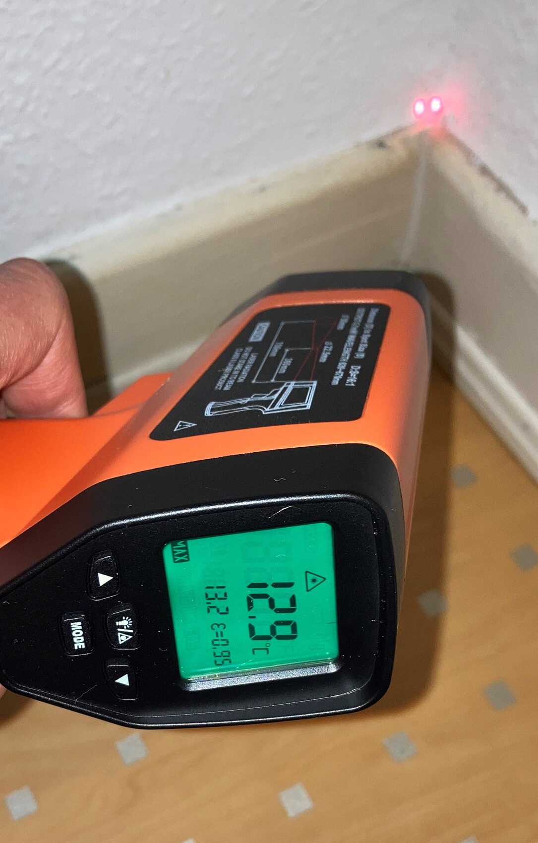 Nahaufnahme eines orange-schwarzen kontaktlosen Messgeräts mit grünem Display und Laserpointer, Ziel auf Wand.
