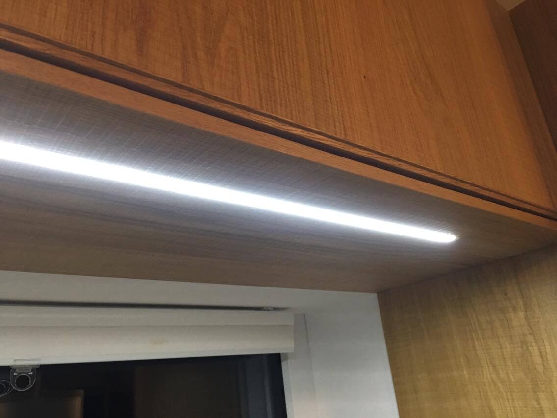 LED-Lichtband unter einem holzfarbigen Oberschrank beleuchtet den Küchenbereich