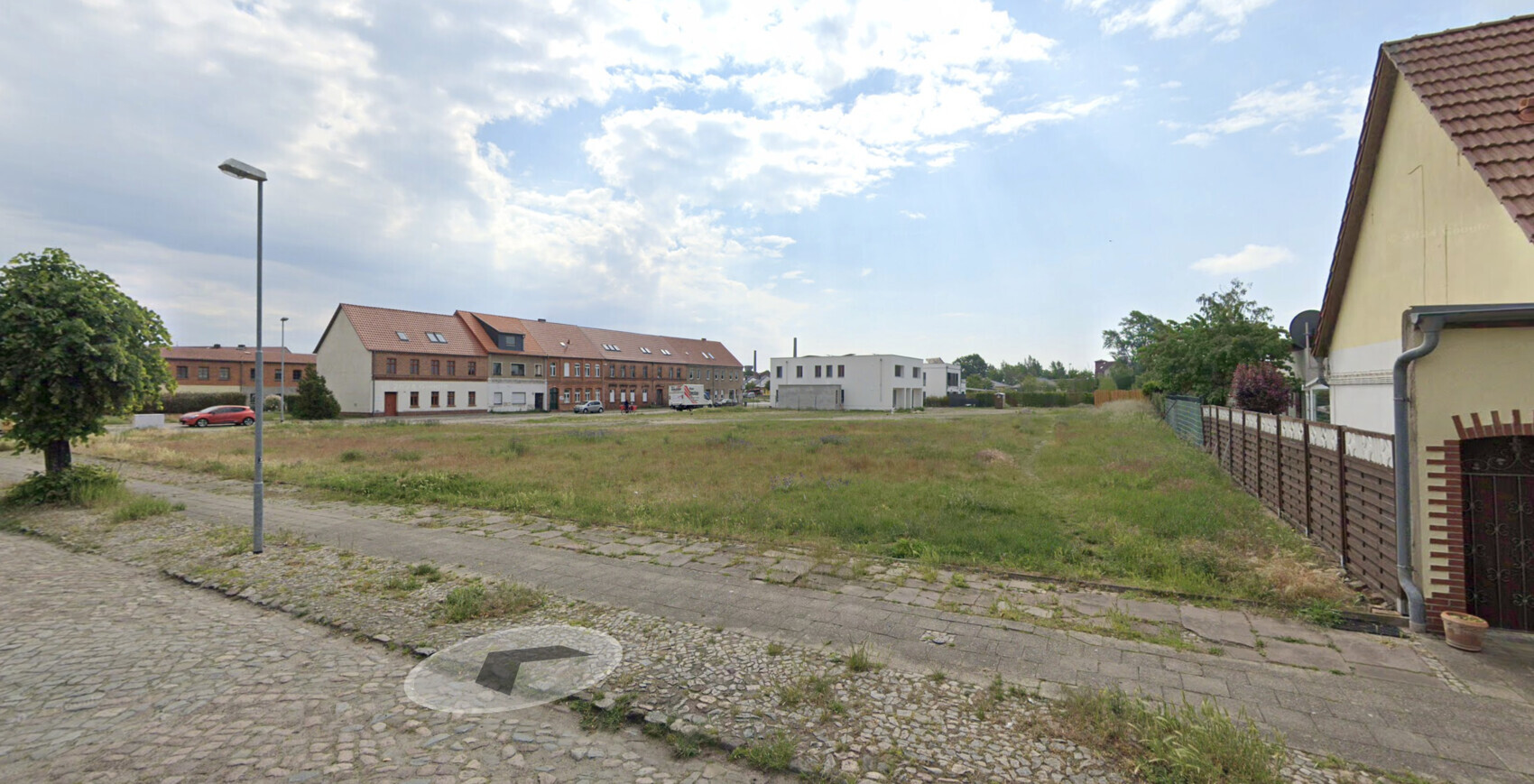Blick auf eine Wohnsiedlung mit roten Ziegelhäusern, Wiese, Laterne und Zaun im Vordergrund
