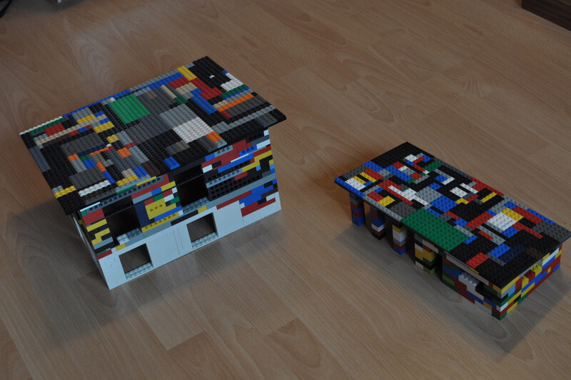 Zwei Lego-Hausmodelle aus bunten Steinen auf Holzboden, detailreiche Daecher.