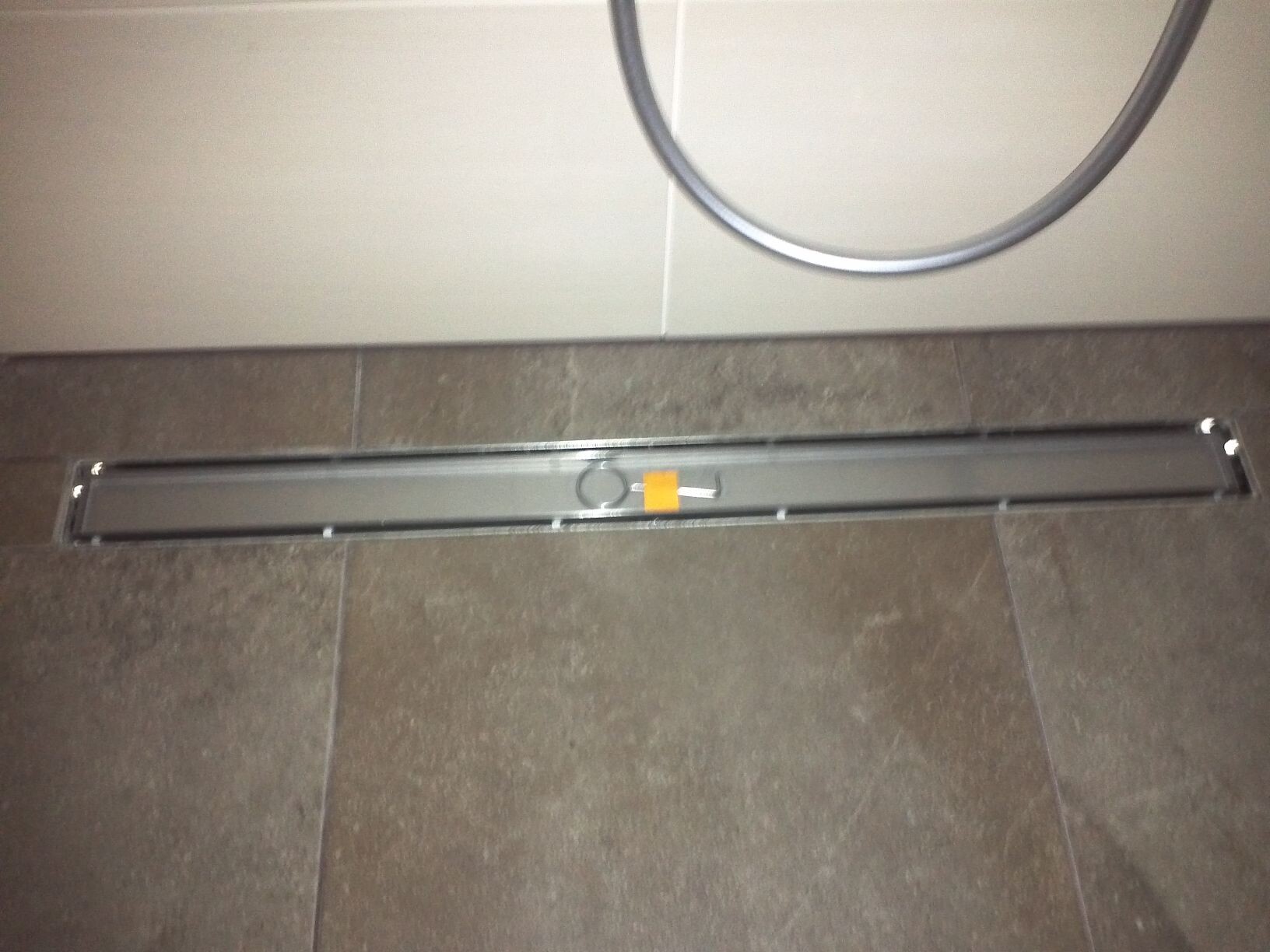 Lange silberne Duschrinne in Bodenfliesen, mittig orange markiert.