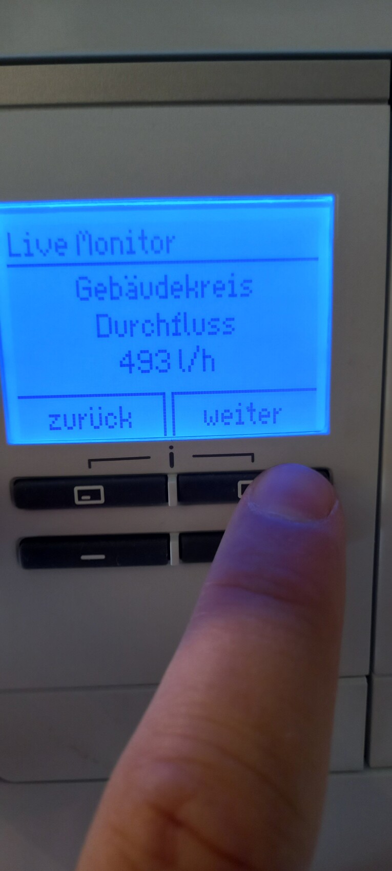 Blaue LCD-Anzeige: Live Monitor; Durchfluss 493 L/h; Knopf zurück/weiter, Finger drückt
