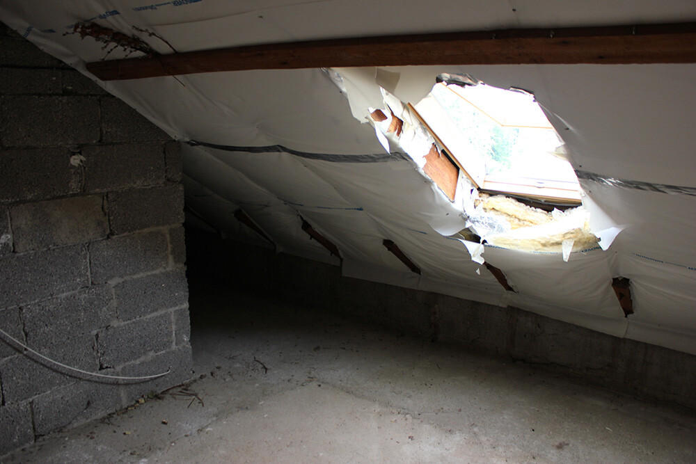 Dachboden mit Loch im Dach, sichtbare Dämmung und Baustoffe an der Decke.