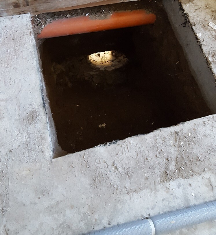 Offenes Loch im Fundament im Boden mit Rohrverlegung auf einer Baustelle.