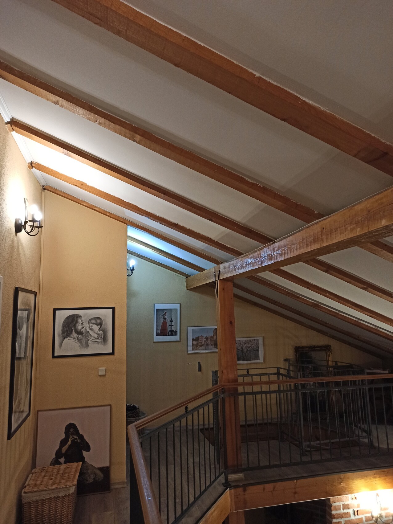 Dachboden-Galerie: Holzbalken-Decke, Geländer, gerahmte Bilder an gelber Wand