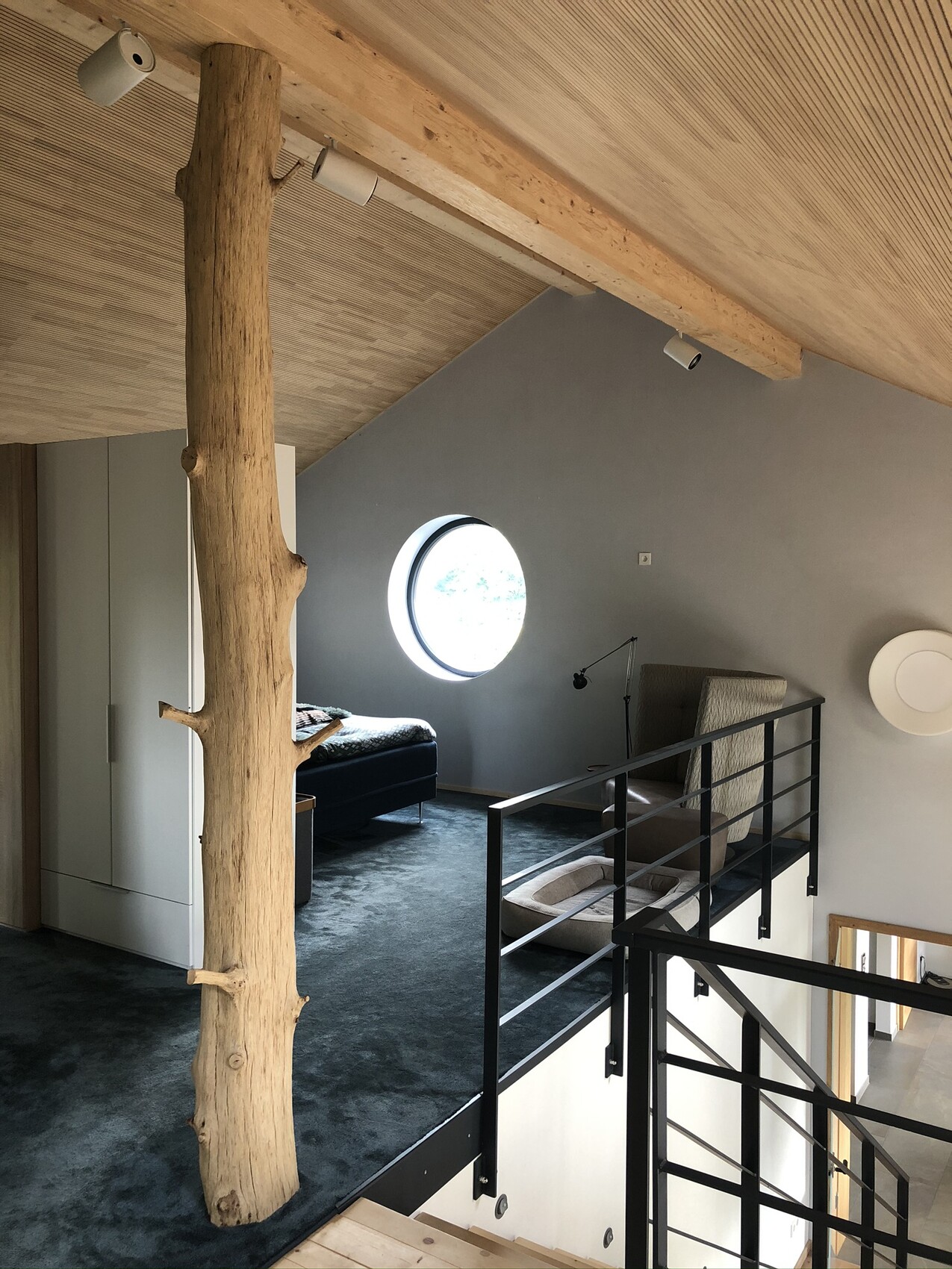 Loft mit Baumstamm als Stütze, runder Fenster, Bett und Lesesessel.