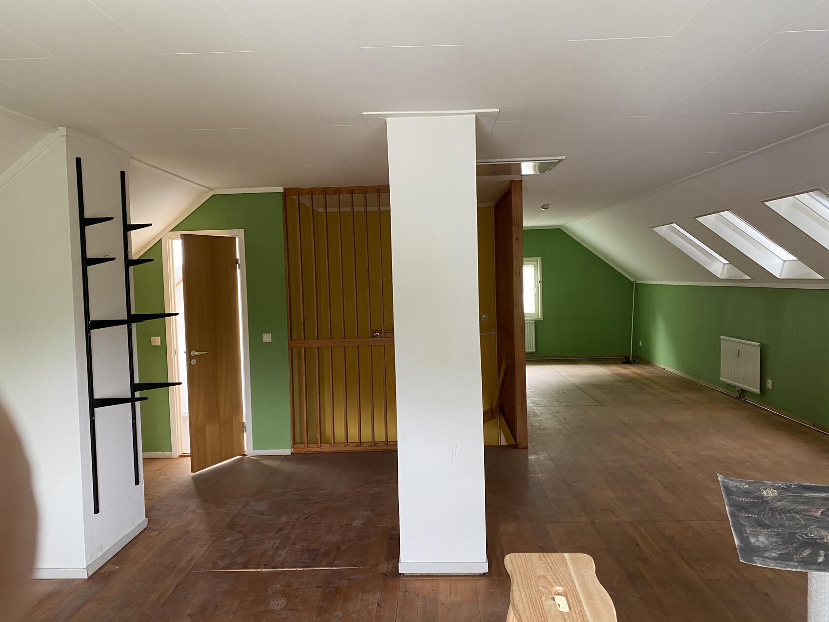Großer Loftraum mit grünen Wänden, zentraler weißer Säule, Treppe, Dachfenstern und Holzboden.
