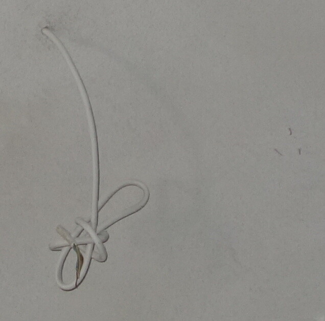Weißes Kabel hängt lose an der Wand, Kabelende mit Knoten sichtbar