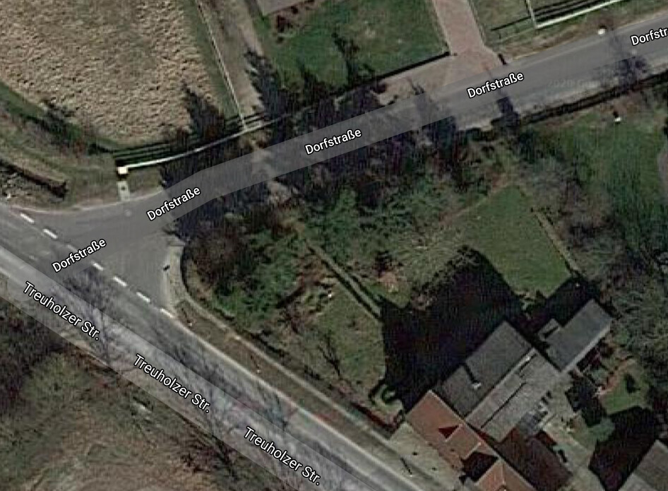 Satellitenbild einer Dorfkreuzung mit Häusern, Bäumen und Feldern.