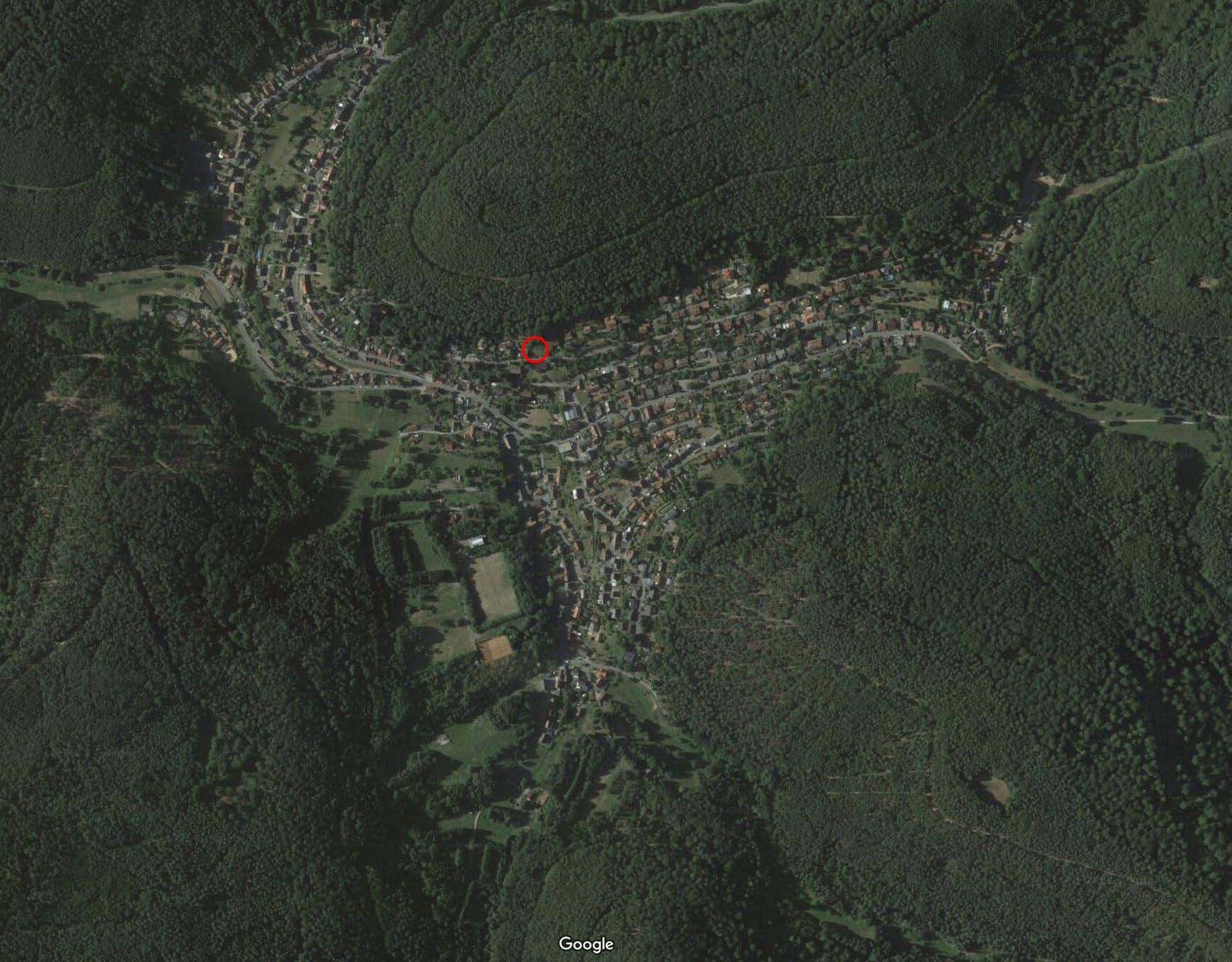 Luftbild eines kleinen Dorfes im Wald; rote Markierung markiert einen Ort an der Hauptstraße.