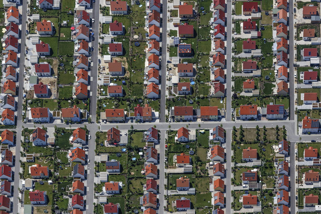 Luftaufnahme eines Wohnviertels mit vielen roten Dächern, grünen Gärten und geradlinigem Straßenraster.
