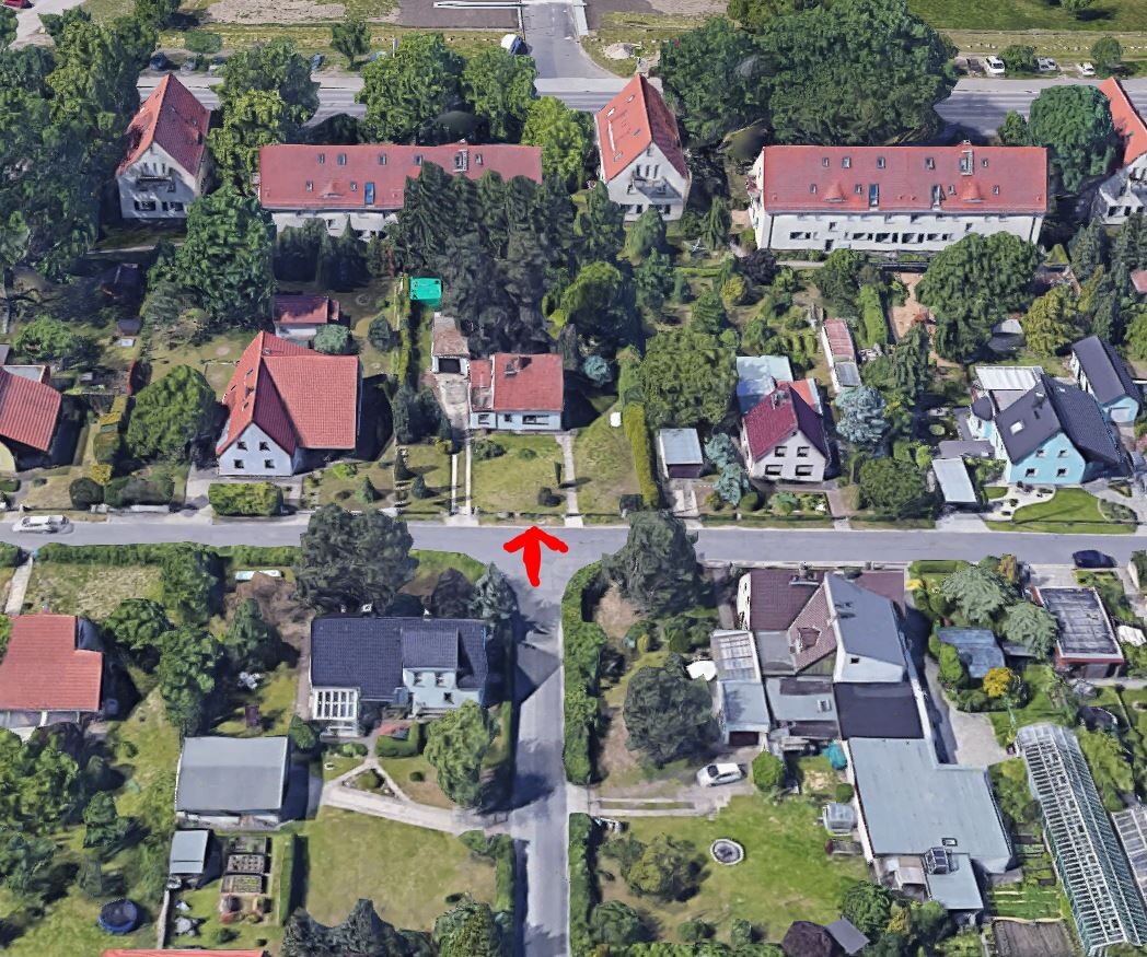 Luftbild eines Wohnviertels mit roten Dächern; roter Pfeil markiert den Straßenzugang.