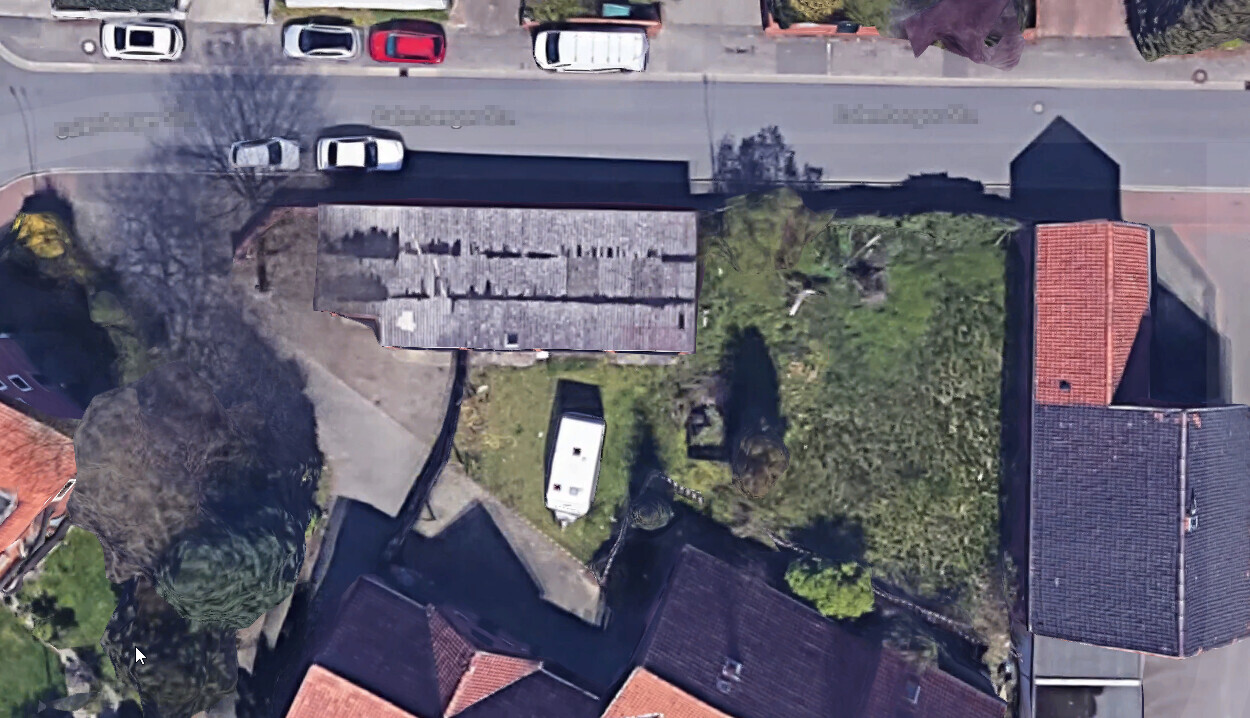 Luftaufnahme einer Wohnstraße mit geparkten Autos, Gebäuden und grünem Garten, Wohnwagen sichtbar.