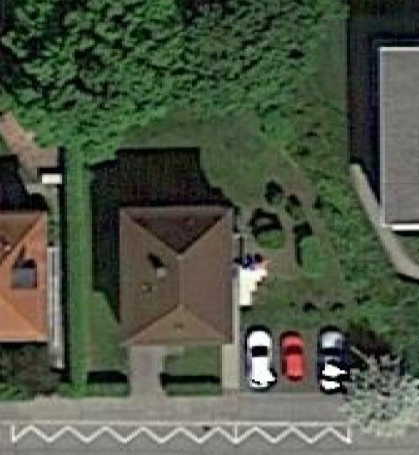 Luftaufnahme eines Hauses mit Garten, drei Autos im Vorgarten, umliegende Häuser.