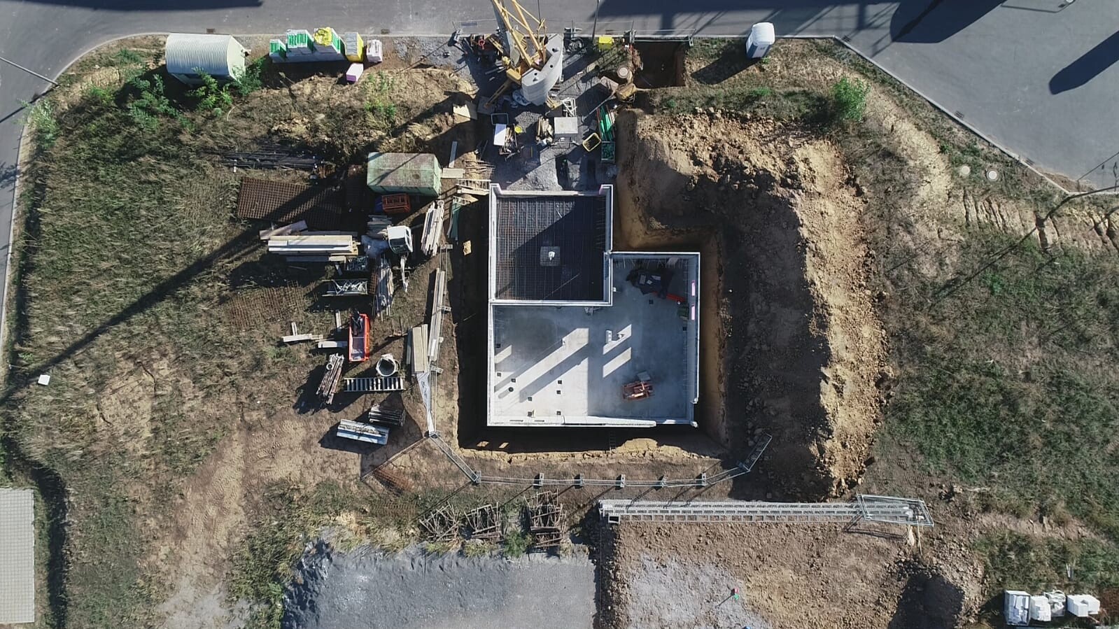 Luftaufnahme einer Baustelle mit Fundamentarbeiten, Kran und Baumaterialien