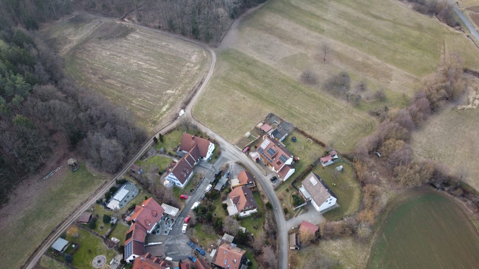 Luftbild einer kleinen Ortschaft: Häuser, Straßen, Felder und Wald am Rand.
