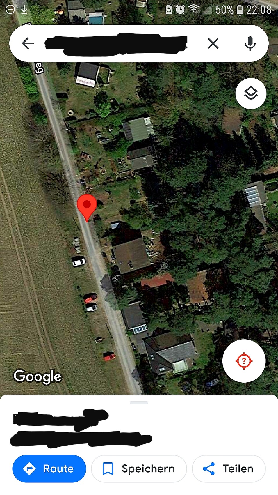 Satellitenansicht einer Wohnsiedlung am Feldrand; roter Lagepin auf der Straße.
