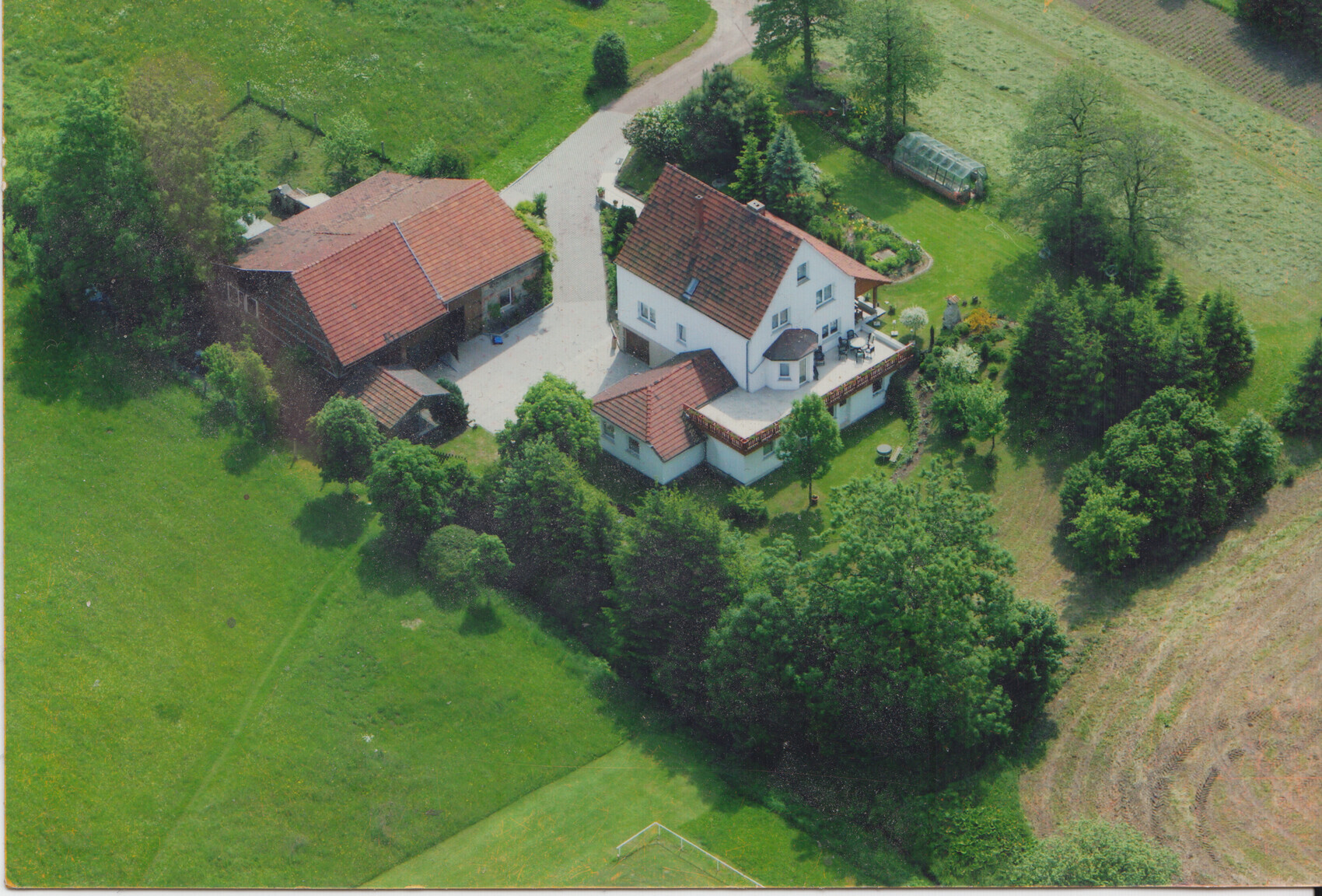 Vogelperspektive: Weißes Haupthaus mit rotem Ziegeldach, Nebengebäuden, Garten und Wiesen.