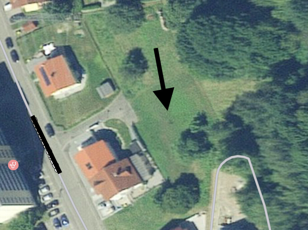 Luftbild einer Wohnsiedlung mit roten Dächern, Grünflächen und einem Pfeil, der Gras zeigt.