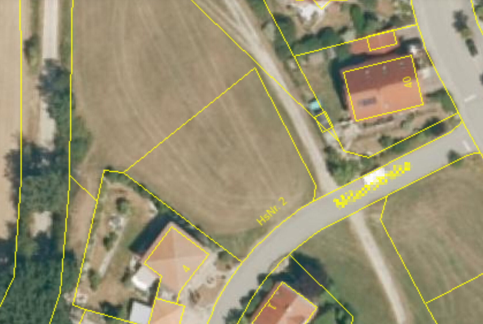 Luftbild eines Wohngebiets mit roten Dächern, Straßen und gelb markierten Parzellen.