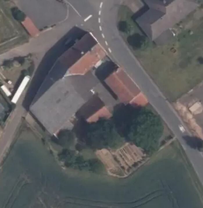Luftbild: kurvige Straße, Häuser mit roten Dächern, Bäume und Gartenfläche.