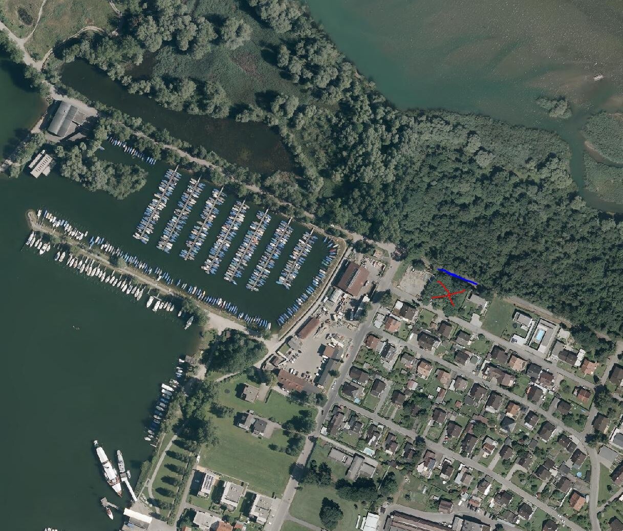Luftbild eines Hafens mit Marina voller Boote neben Wohnhäusern und Grünflächen