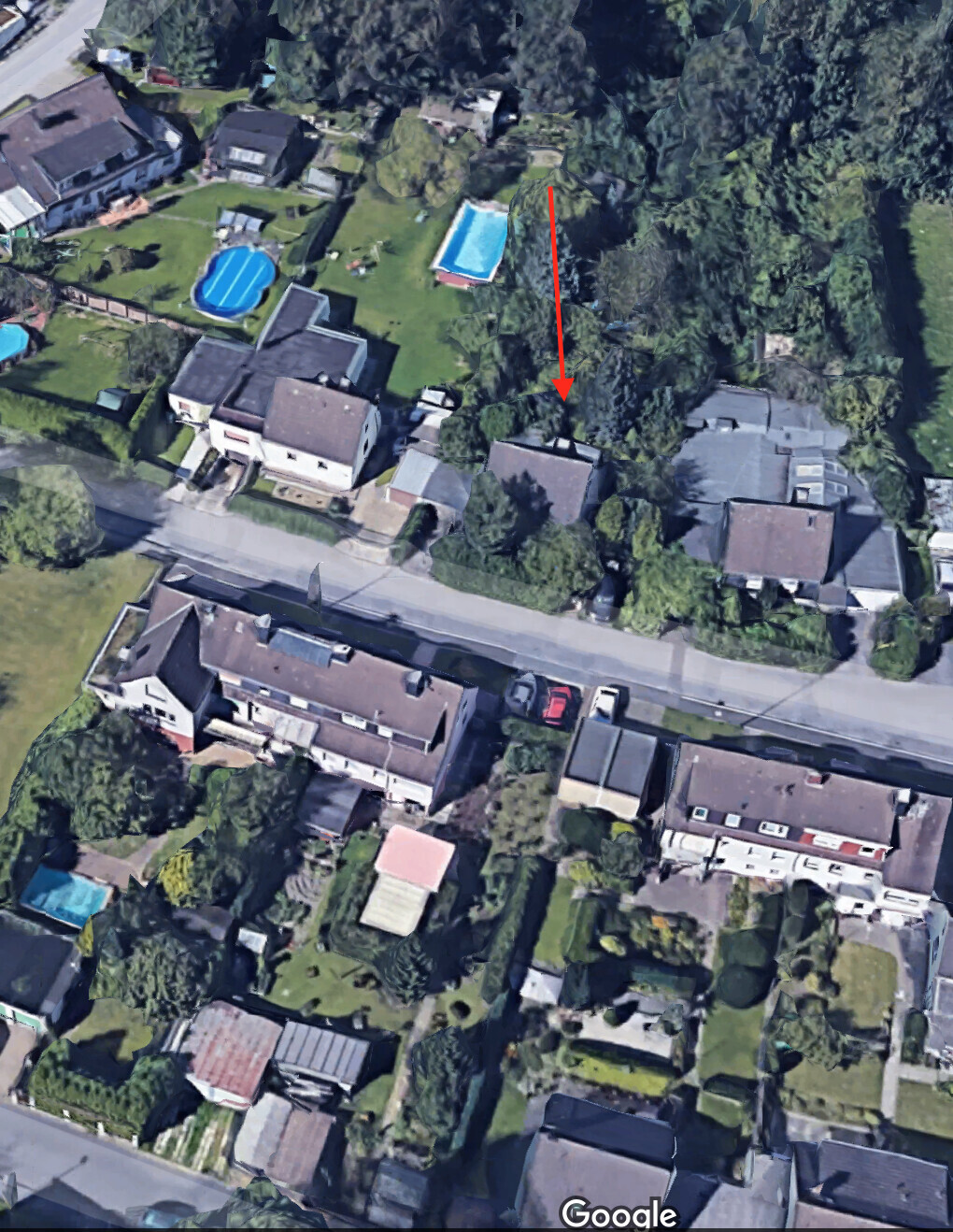 Luftbild einer Vorstadt mit Häusern, Gärten und Pools; roter Pfeil zeigt auf ein Haus.
